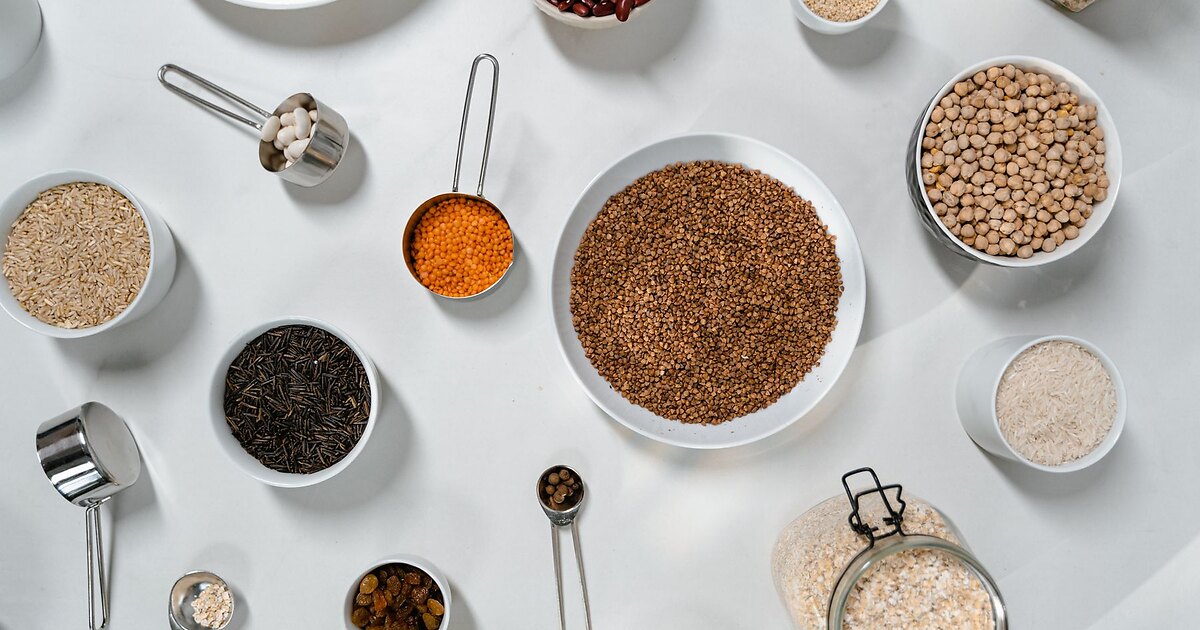 Overhead flat-lay of grains and legumes for Intestinal body type meal prep — brown and white rice, wild rice, buckwheat, chickpeas, red lentils, kidney beans, oats, and raisins in white bowls and jars
